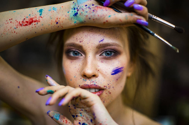 portrait of a woman artist with a drops of paints on the face ah hands. brushes in the hand, - Foto, Imagem