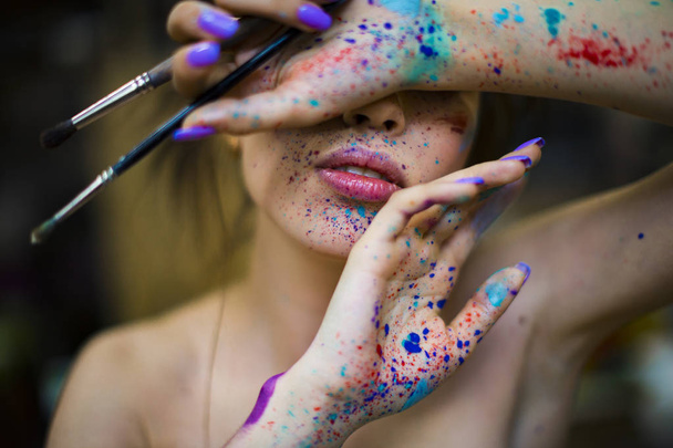 portrait of a woman artist with a drops of paints on the face ah hands. brushes in the hand - Фото, зображення