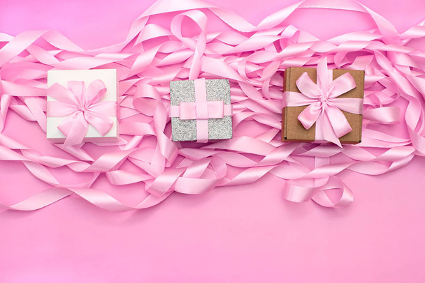 Three boxes with gifts on the background of the revolution of decorative satin ribbons of pink color. - Photo, Image