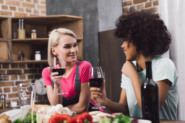 multiethnic girls talking with wine in kitchen - Foto, afbeelding
