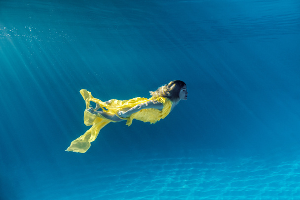 υποβρύχια φωτογραφία του όμορφη νεαρή γυναίκα με φόρεμα κολύμπι στην πισίνα - Φωτογραφία, εικόνα