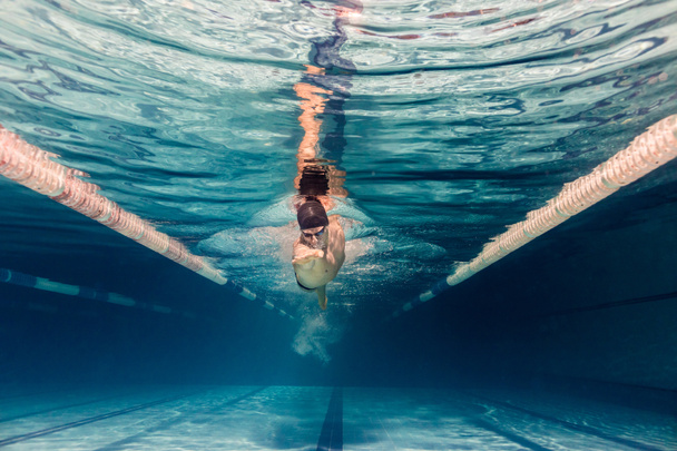 underwater picture of young swimmer in cap and goggles training in swimming pool - Photo, Image