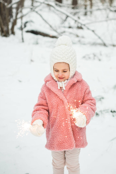 little girl is holding bengal lights in the winter in forest - Foto, imagen