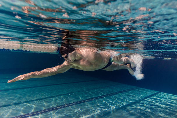 underwater picture of young swimmer in cap and goggles training in swimming pool - Photo, Image