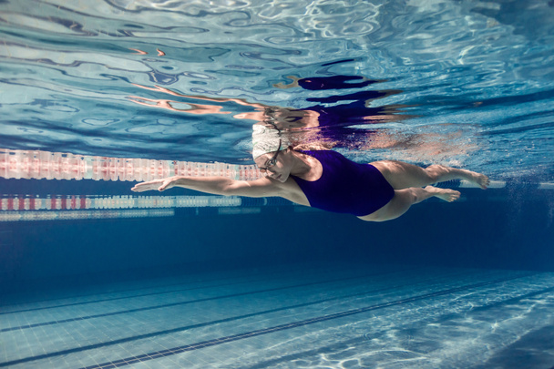 underwater picture of female swimmer in swimming suit and goggles training in swimming pool - Photo, Image