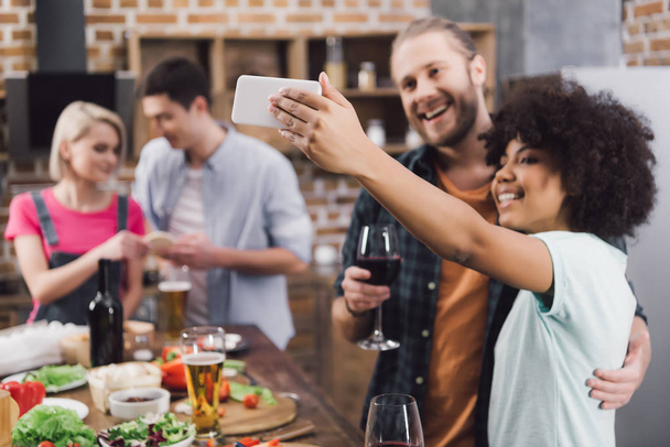 amici multietnici scattare selfie in cucina con smartphone
 - Foto, immagini