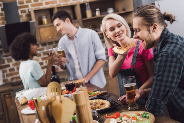 мультикультурные друзья едят домашнюю пиццу и пьют алкоголь дома
 - Фото, изображение