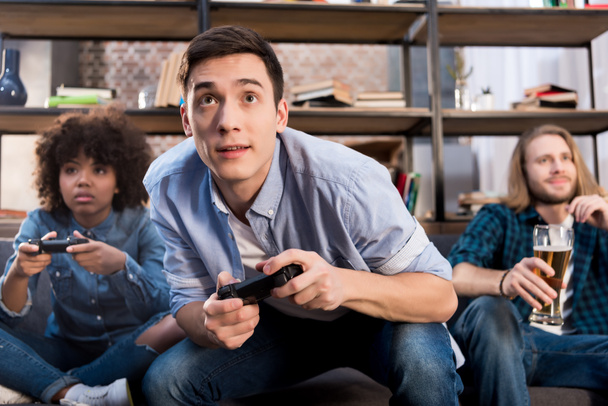 мультикультурные друзья играют в видеоигры на диване дома
 - Фото, изображение