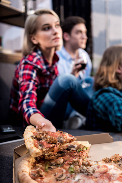 chica tomando pedazo de pizza mientras pasar tiempo con amigos
 - Foto, imagen