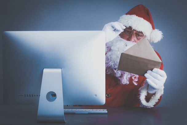 Santa Claus leyendo cartas de los niños y escribiendo respuestas a ellos usando el ordenador portátil
 . - Foto, imagen