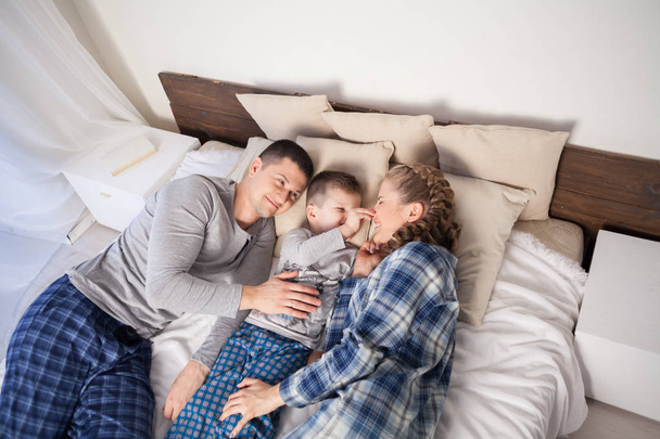 mom dad and son in the morning lying on the bed at home - Photo, Image