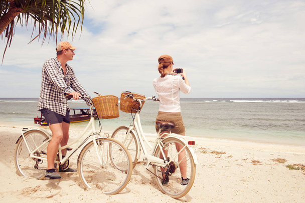 Coppia felice scattare foto guarda il mare in piedi vicino alle loro biciclette vecchio stile sulla spiaggia theon
.  - Foto, immagini