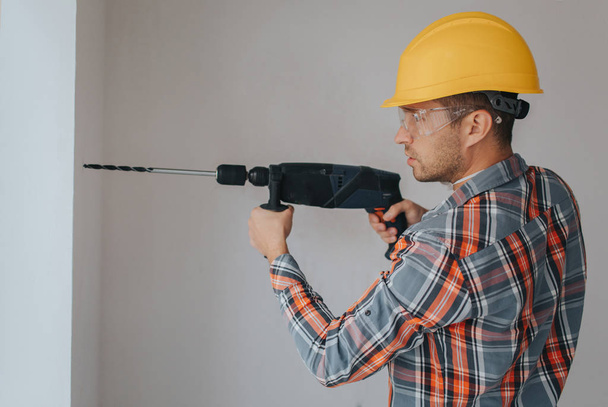 Ouvrier constructeur avec équipement faisant un trou dans le mur sur le chantier de construction
 - Photo, image