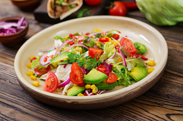 Appetizing vegan salad from tomatoes, avocado, corn, red onion and lettuce leaves. Tasty vegan food. Healthy vegan food. Vegetarian salad. - Photo, Image