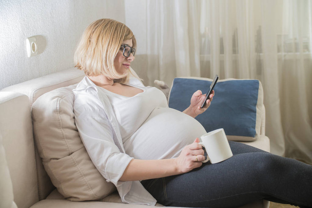 zwangere vrouw thuis met telefoon - Foto, afbeelding
