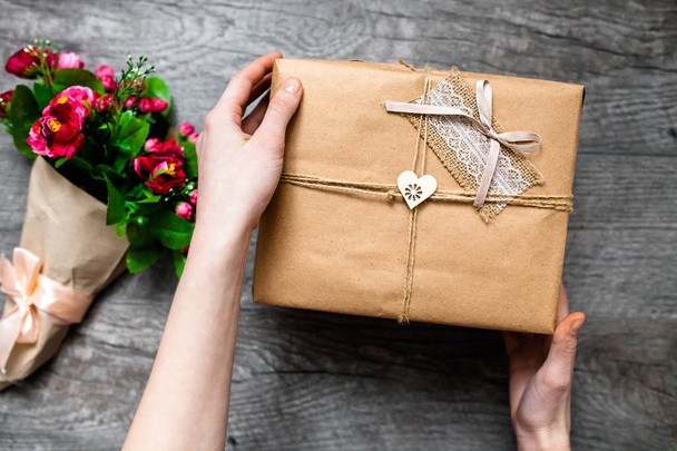 Female hand holding a wrapped gift ,Valentine's Day, romantic photo . Romantic grey wooden background with hearts and gifts, suitable for advertising - 写真・画像