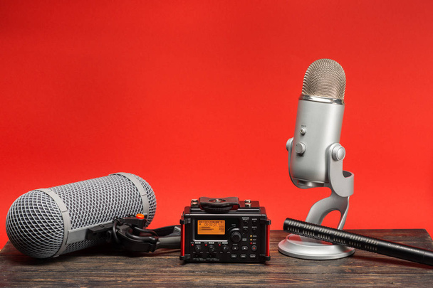Ausrüstung für Feldaudioaufnahmen auf rotem Hintergrund. Richtmikrofon, USB-Mikrofon, Rekorder und Windschutzscheibe - Foto, Bild