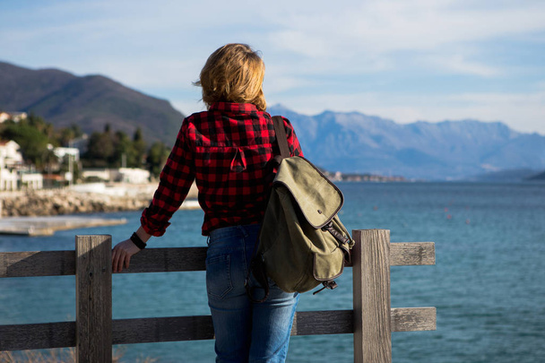 Woman in a shirt with a backpack is standing on a wooden pier - Photo, image
