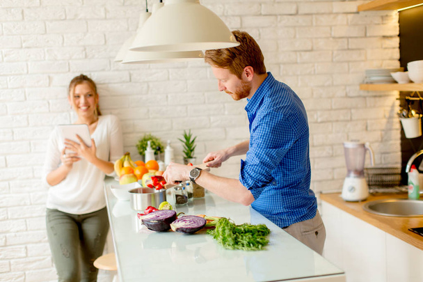 Onnellinen nuori pari pitää hauskaa modernissa keittiössä sisätiloissa valmistellessaan vihanneksia ruokaa lounaaksi
 - Valokuva, kuva