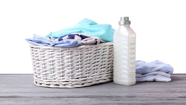 Basket with dirty clothes and laundry detergent on table against white background - Foto, imagen
