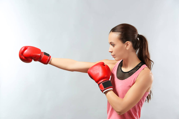 Strong woman in boxing gloves on grey background - 写真・画像