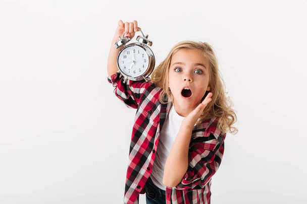 Portrait of a surprised little girl showing alarm clock - 写真・画像