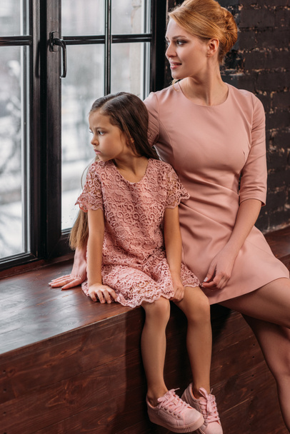 mother and daughter sitting on windowsill and looking at window - Фото, зображення