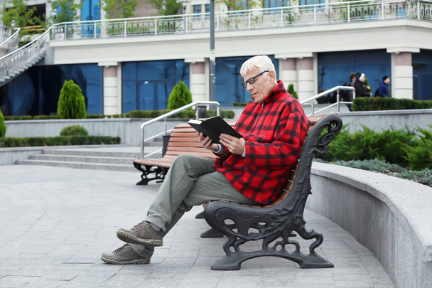 Handsome mature man reading book on bench outdoors - Fotó, kép