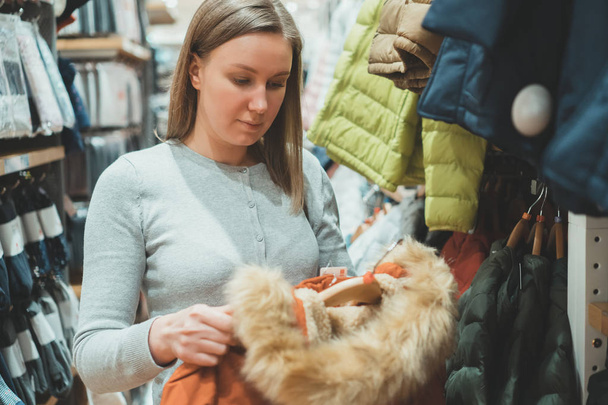 Woman choosing winter jacket with fur in clothing store. - Photo, Image