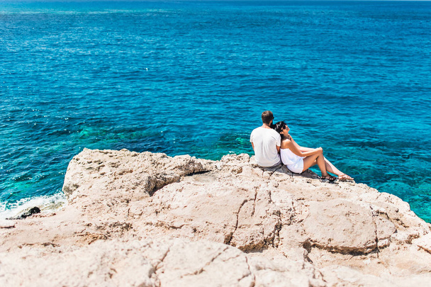 Couple in love by the sea on the rock. Honeymoon lovers. Man and woman traveling. Couple in love on vacation. Newly married couple. Sea tour. Honeymoon trip. The couple on the cliff by the sea - Fotó, kép