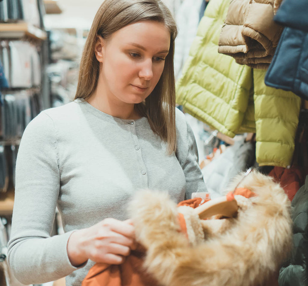 Woman choosing winter jacket with fur in clothing store. - Fotó, kép