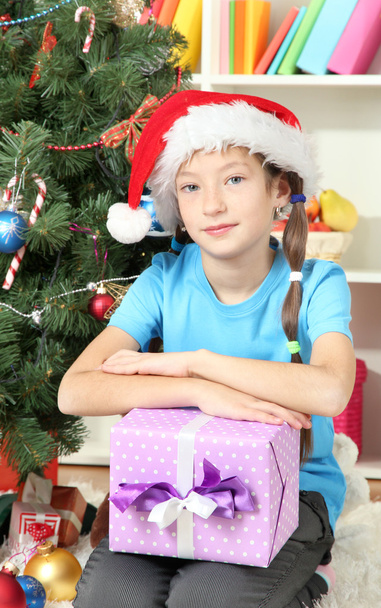 Little girl holding gift box near christmas tree - 写真・画像