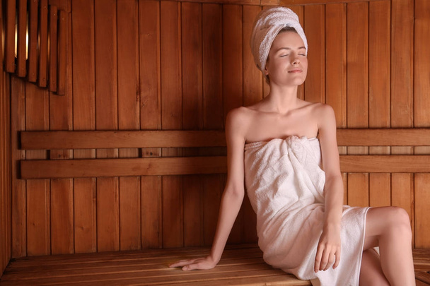 Young woman sitting on wooden bench in sauna - Zdjęcie, obraz
