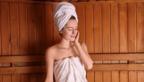 Young woman sitting on wooden bench in sauna - Фото, изображение