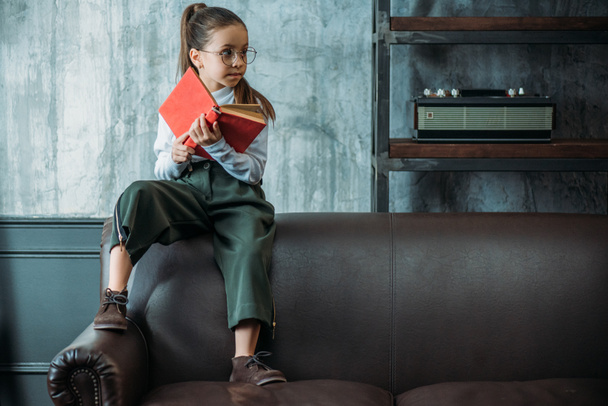 thoughtful little child with book sitting on couch in loft apartments - Fotoğraf, Görsel