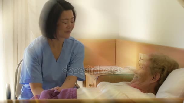zdravotní sestra mluvit starší ženské pacient ležel v posteli v nemocnici - Záběry, video
