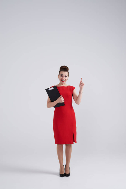 Удивлённая деловая женщина держит папку и указывает вверх
  - Фото, изображение