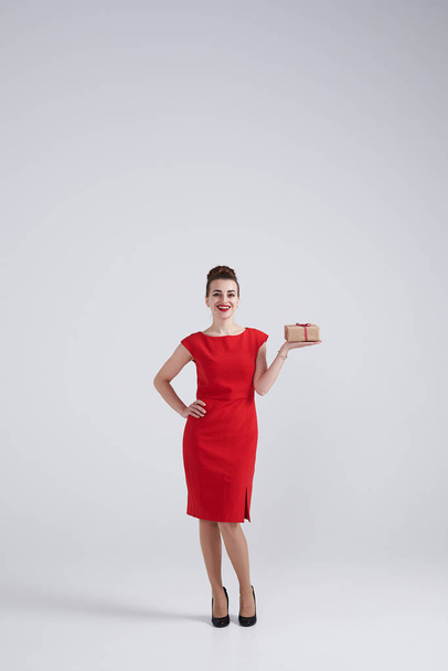 Positive woman in red dress holding present box - Zdjęcie, obraz