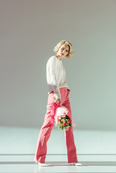 po celé délce pohled krásná blondýnka v růžové oblečení drží kytici a pózuje ve studiu - Fotografie, Obrázek