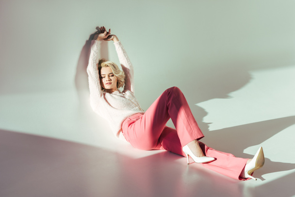 full length view of beautiful young woman in pink clothes lying in studio on grey - Fotó, kép