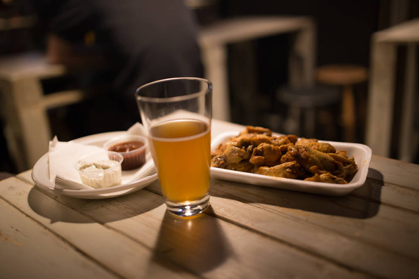 Пиво, куриные крылышки и соус на столе в пабе
 - Фото, изображение