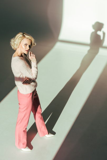 high angle view of beautiful blonde woman in trendy pink clothes looking at camera in studio - Φωτογραφία, εικόνα