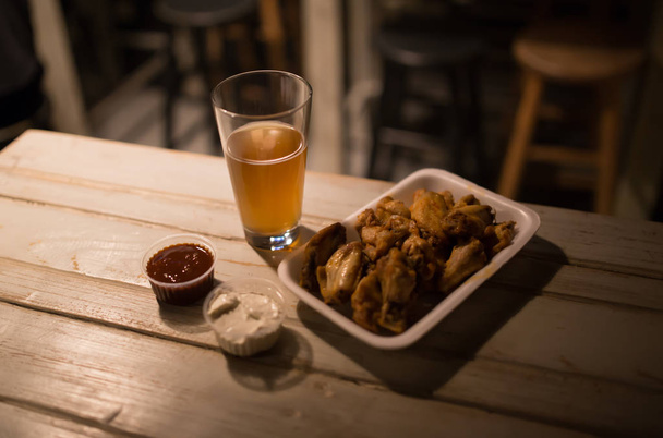 Olutta, kanansiipiä ja kastiketta pubin pöydällä
 - Valokuva, kuva