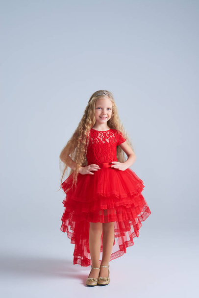 Cute small girl in red ball-dress posing at camera - Fotó, kép