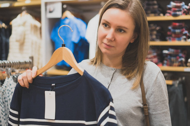 Woman choosing sweater in clothing store. - 写真・画像