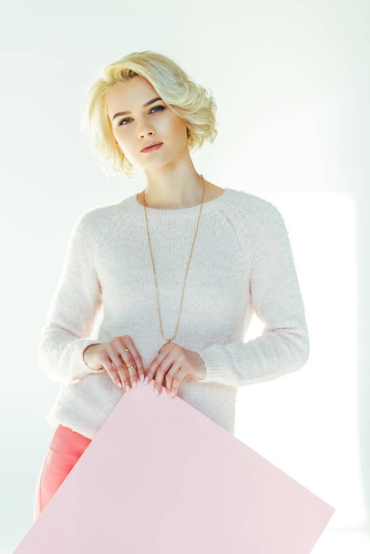 beautiful blonde girl holding pink placard and looking at camera on grey  - Fotografie, Obrázek