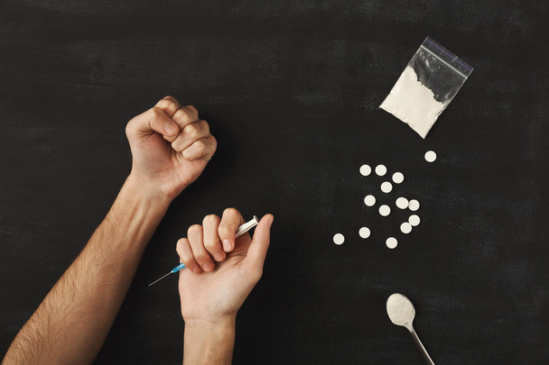 Mãos viciadas em drogas segurando seringa para injeção na mesa escura
 - Foto, Imagem