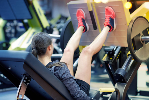 woman flexing muscles on leg press machine in gym - Foto, Imagen