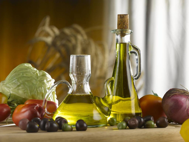 ampolle di vetro di olio d'oliva, olive sparse e verdure. vista frontale sul tavolo della cucina. parete di legno e tenda bianca sono sullo sfondo
. - Foto, immagini