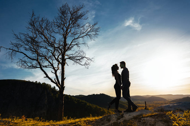 Silhouette of a couple in love. Guy and girl hugging at sunset. Couple travels. Lovers in nature. Man and woman watching the sunset. Lovers at sunset. Travel in the mountains. Honeymoon trip - Foto, imagen